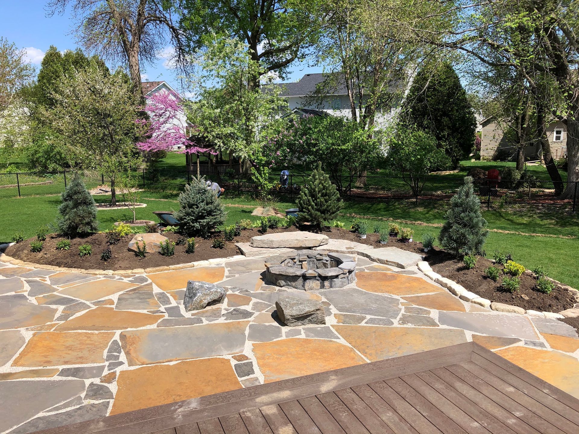 Stone patio with fire pit surrounded by landscaping and trees.