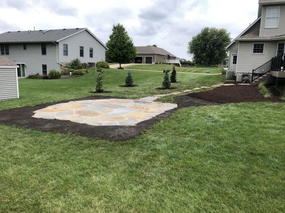 Stone patio in a backyard, surrounded by grass, with trees and houses in the background.