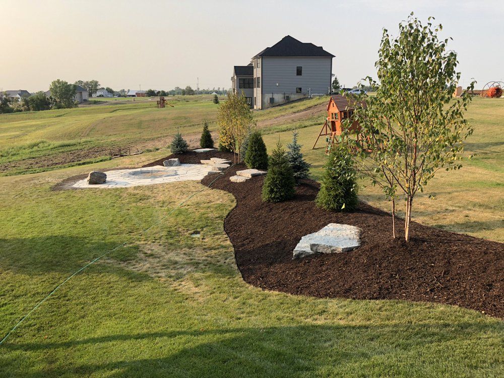 Landscaped backyard with fire pit and trees, brown mulch border.