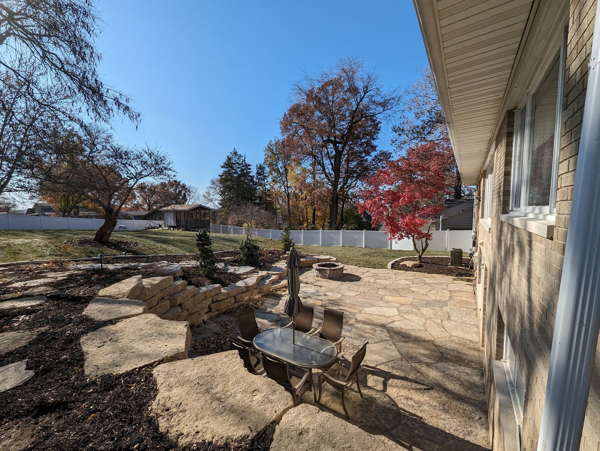 Backyard patio with stone pavers, dining set, and fall foliage.