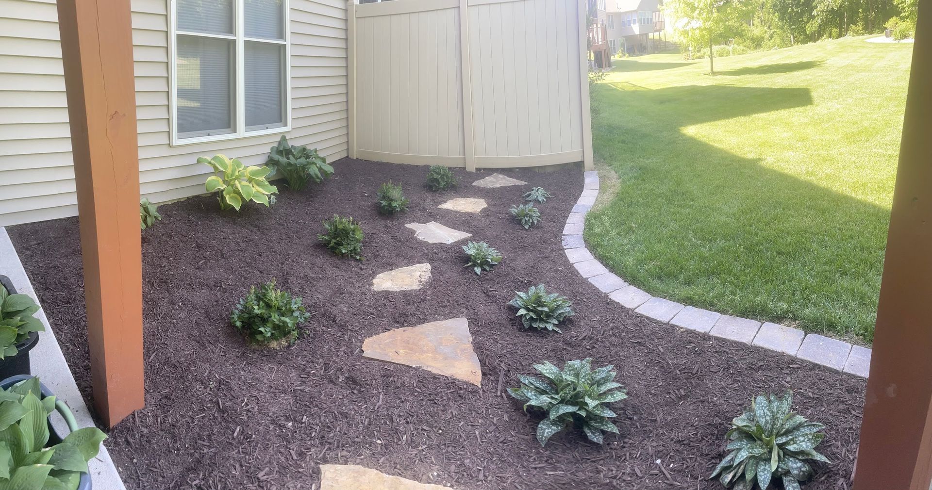 A flower bed with a stone pathway, plants, and mulch.