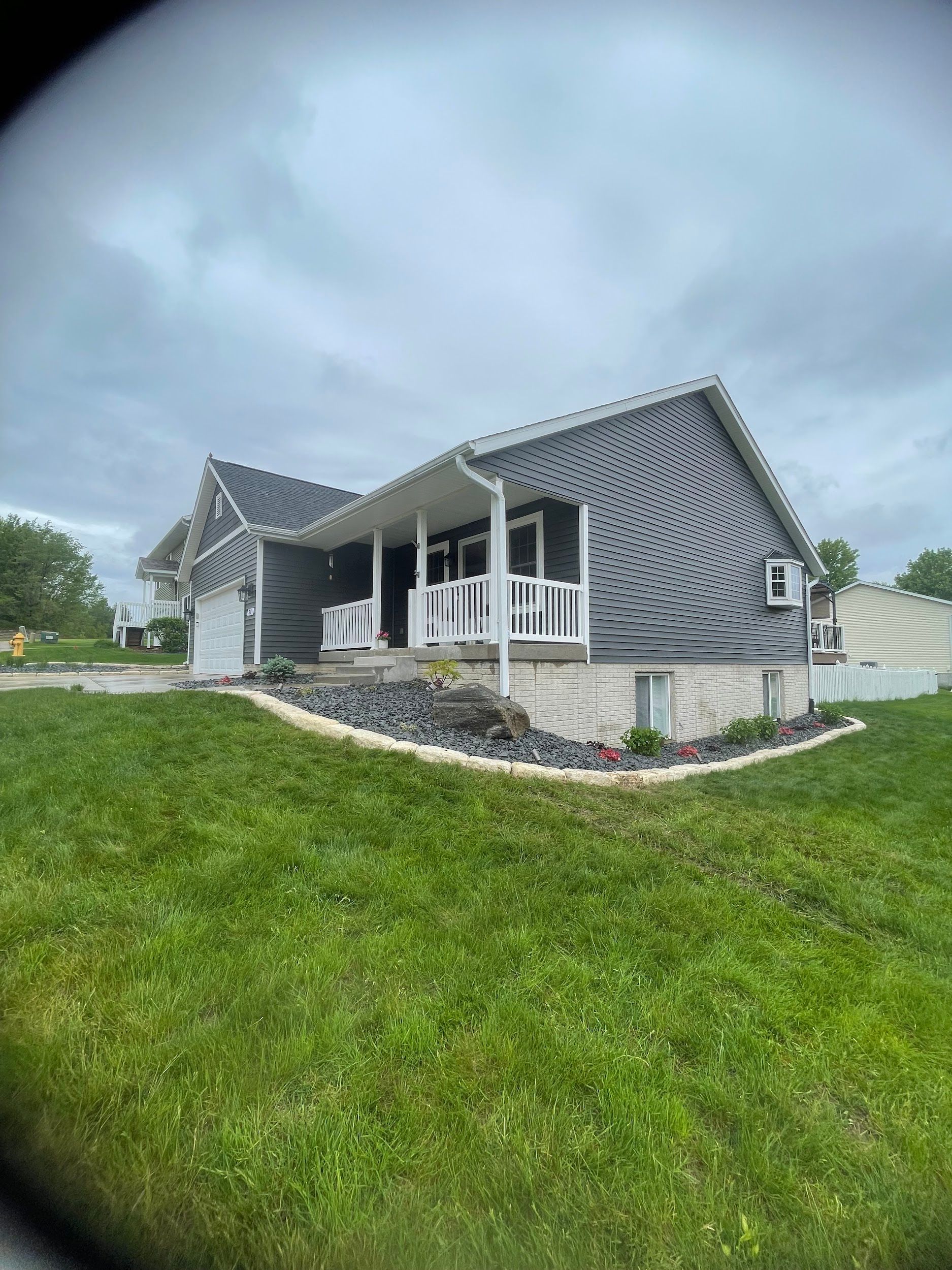 Gray house with white trim and porch, on a grassy lawn under a cloudy sky.