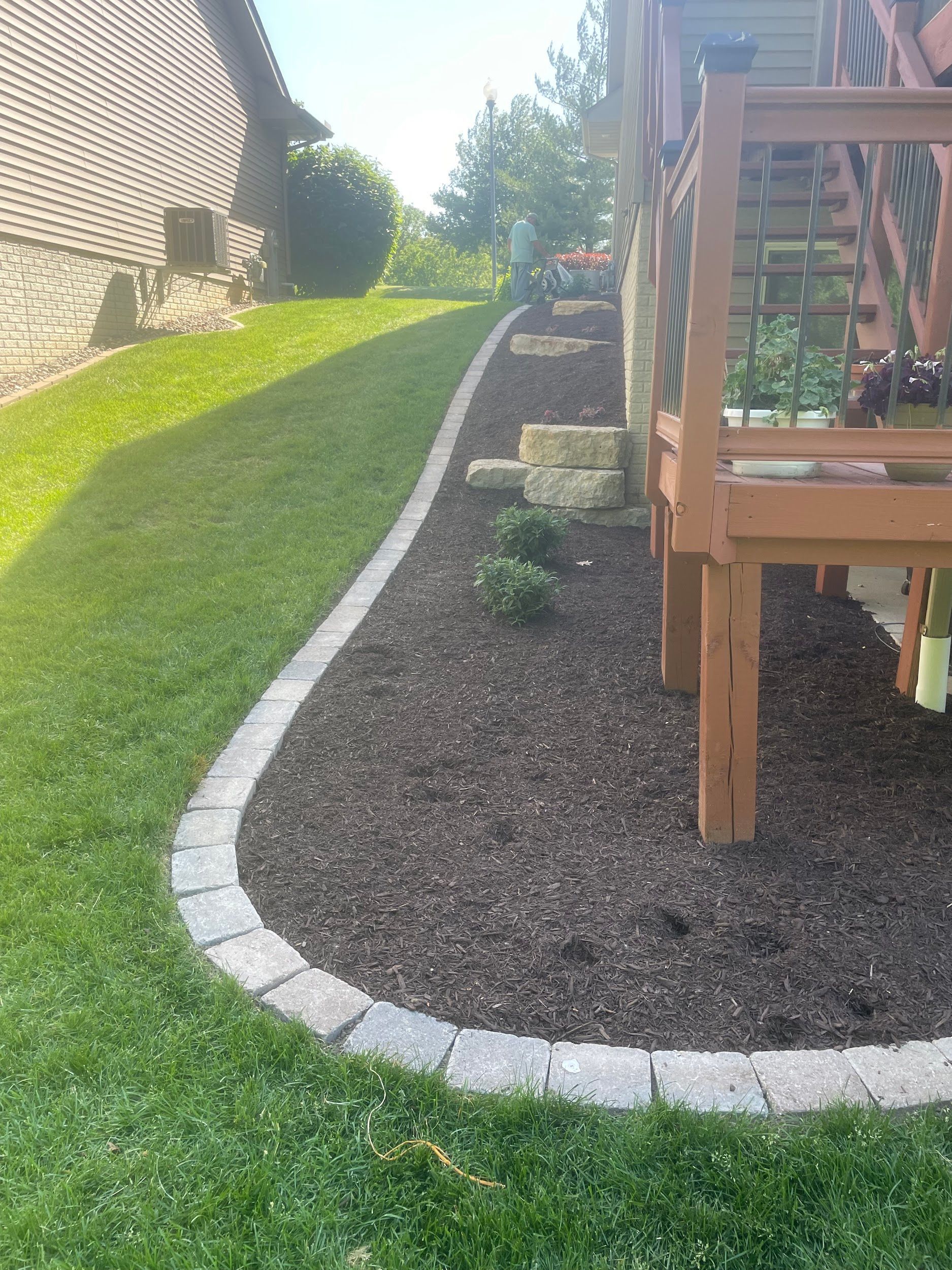 Lawn with curved stone edging borders a mulch bed next to a wooden deck.