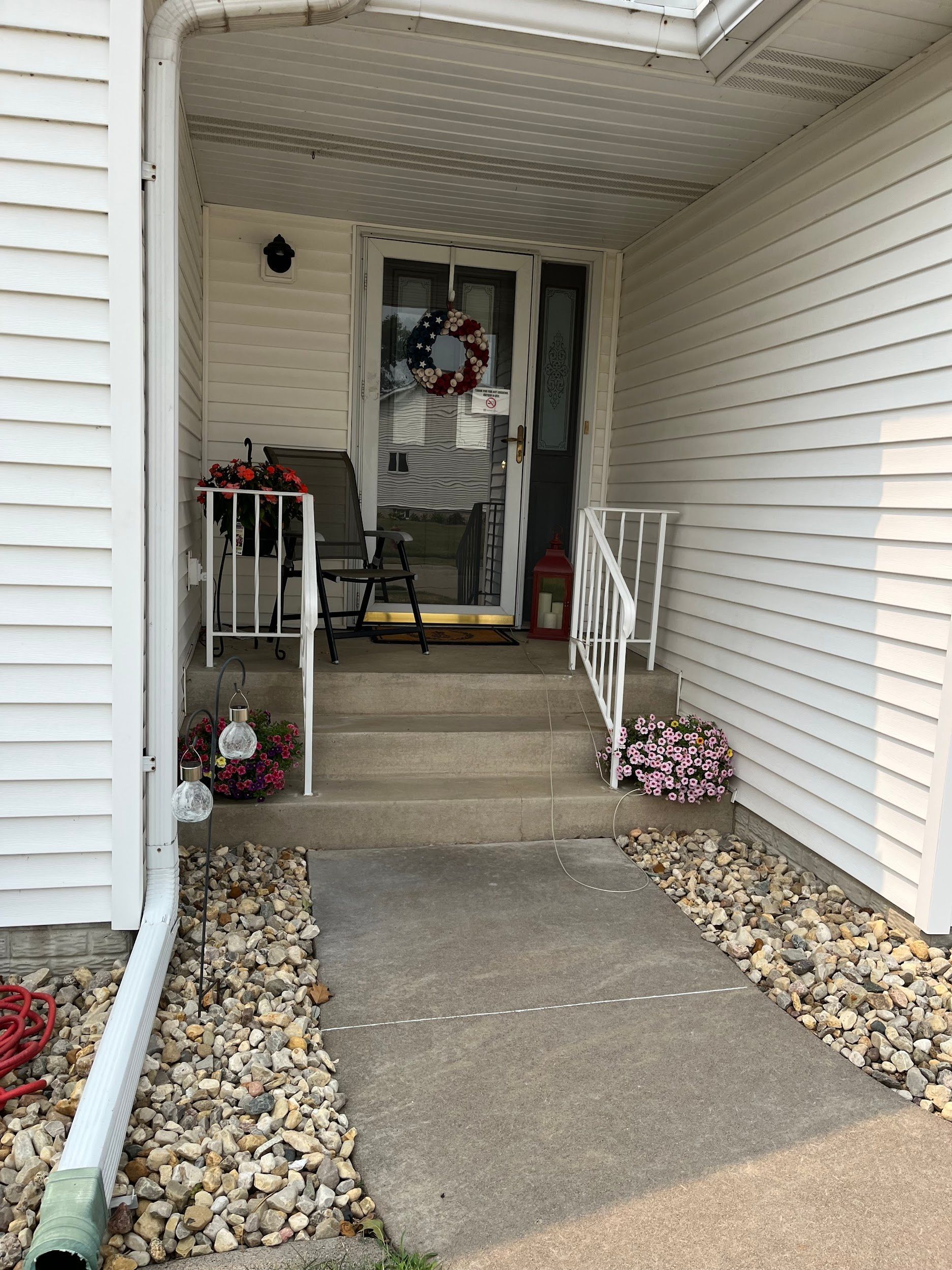 Concrete steps leading to a house entrance with white siding, a wreath, and a small porch.