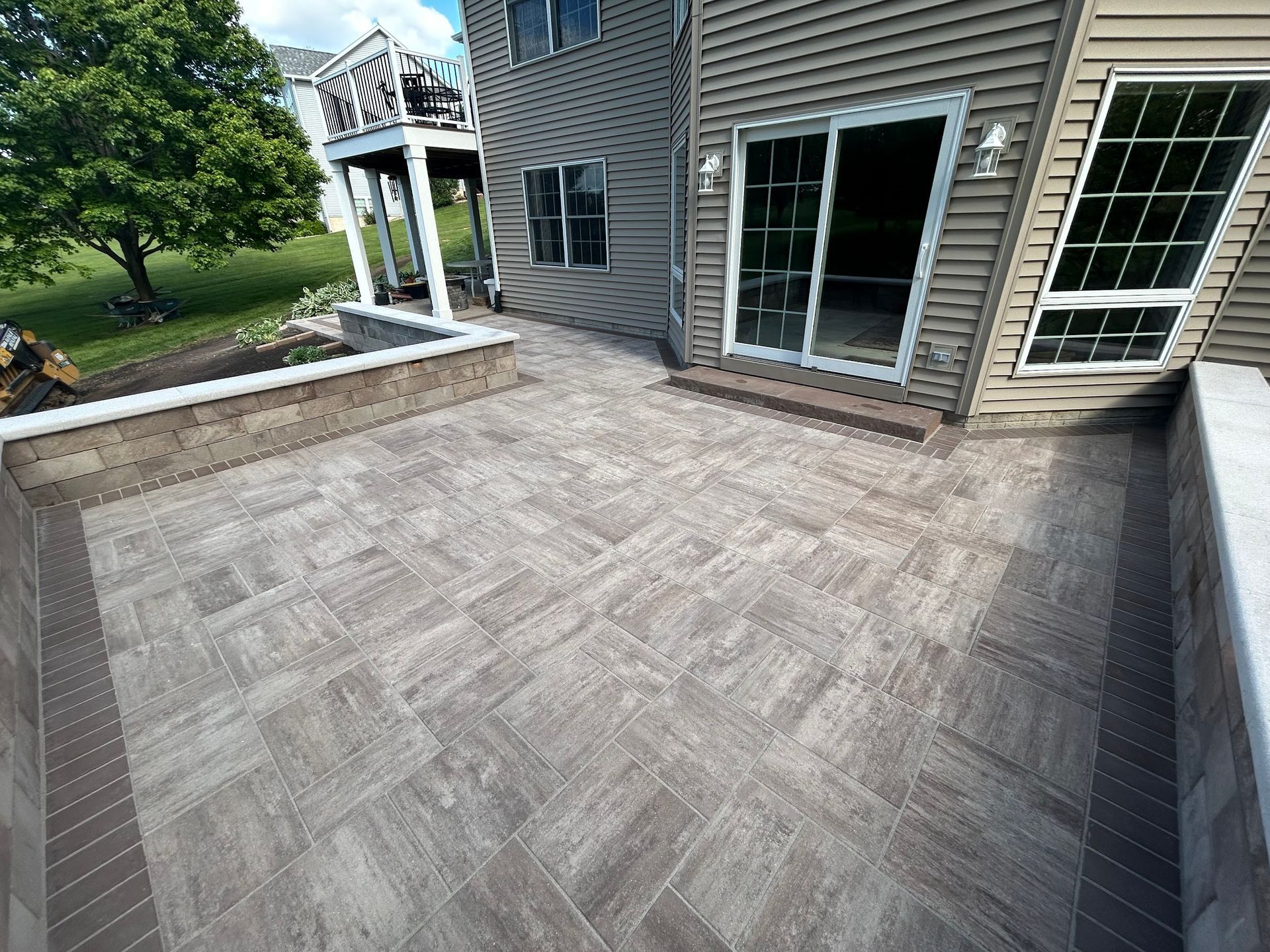 Paver patio with brown border, next to a house with a sliding glass door.