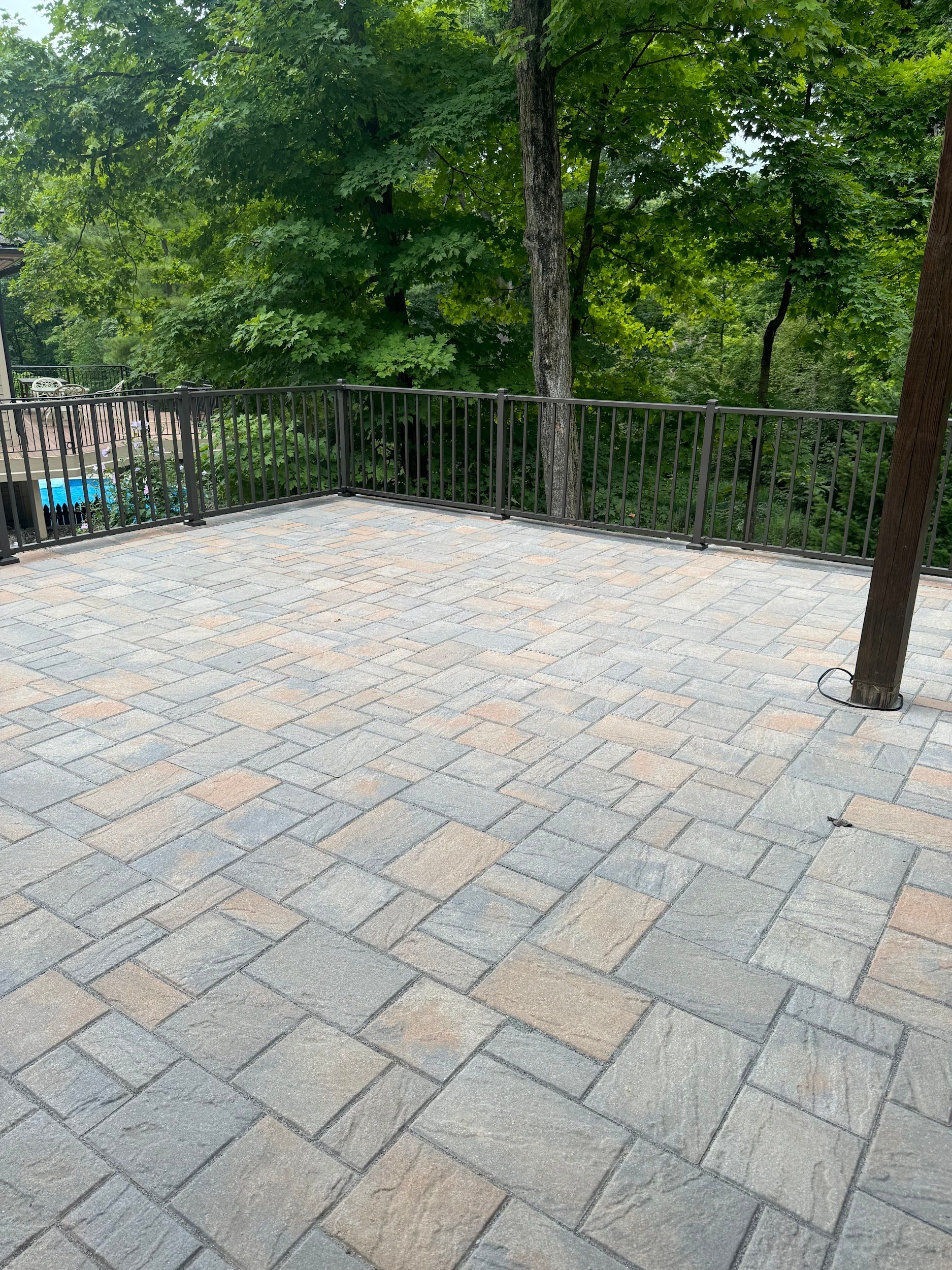 Patio with patterned paving stones, surrounded by a metal railing and trees in a wooded setting.