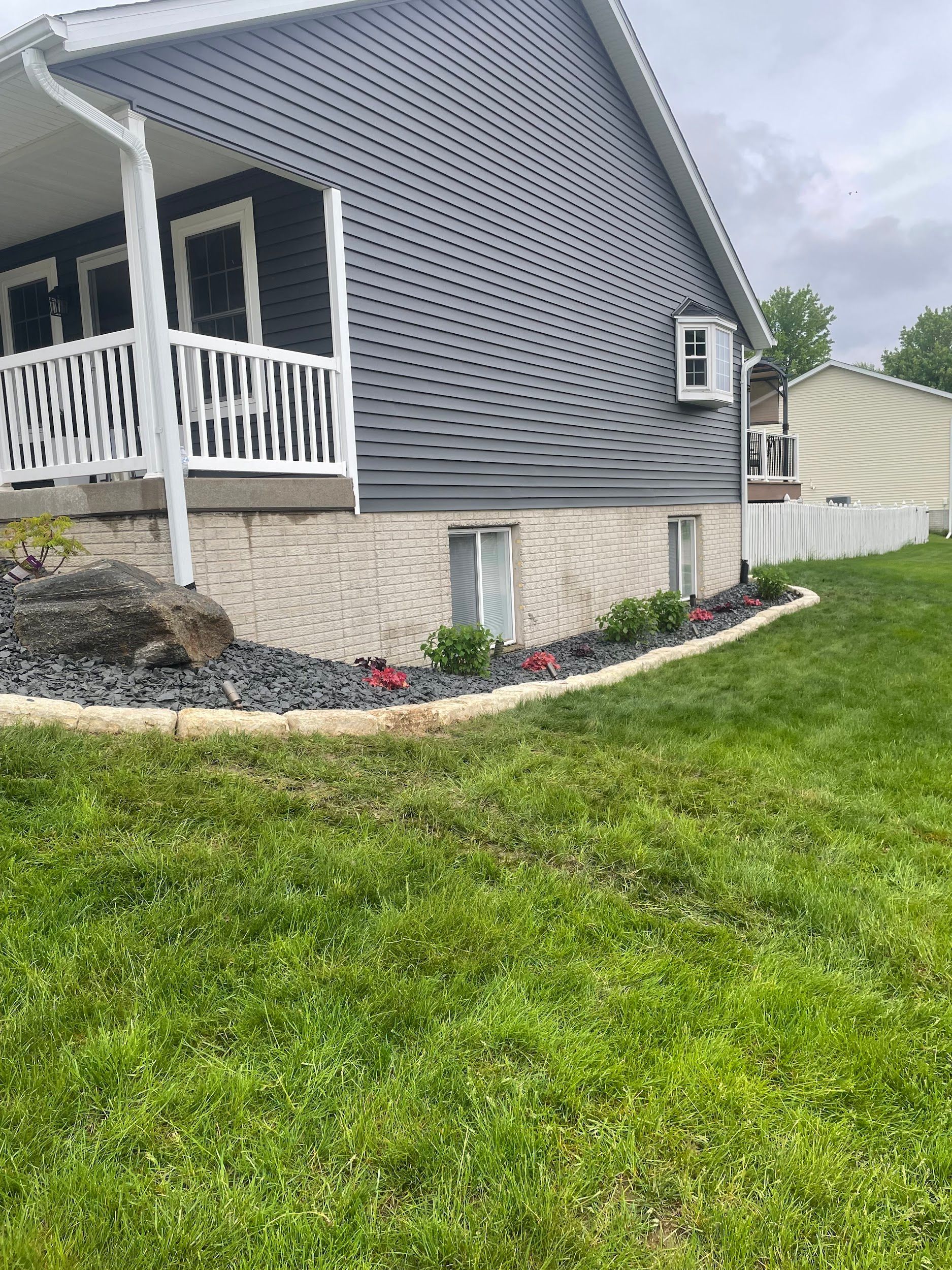 House with dark blue siding, white trim, and a brick foundation; a lawn in the foreground.