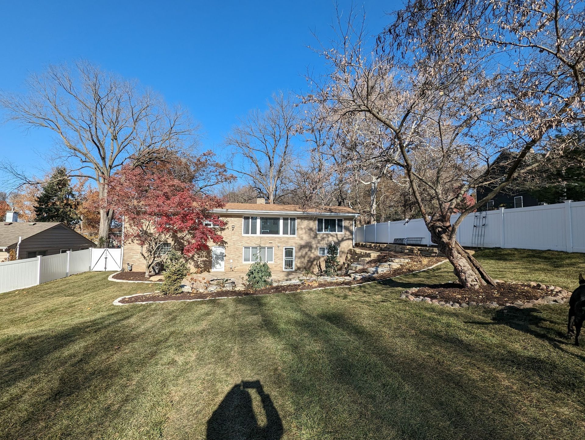 House with landscaping and fall foliage, viewed from a slightly elevated grassy yard; sunny day.