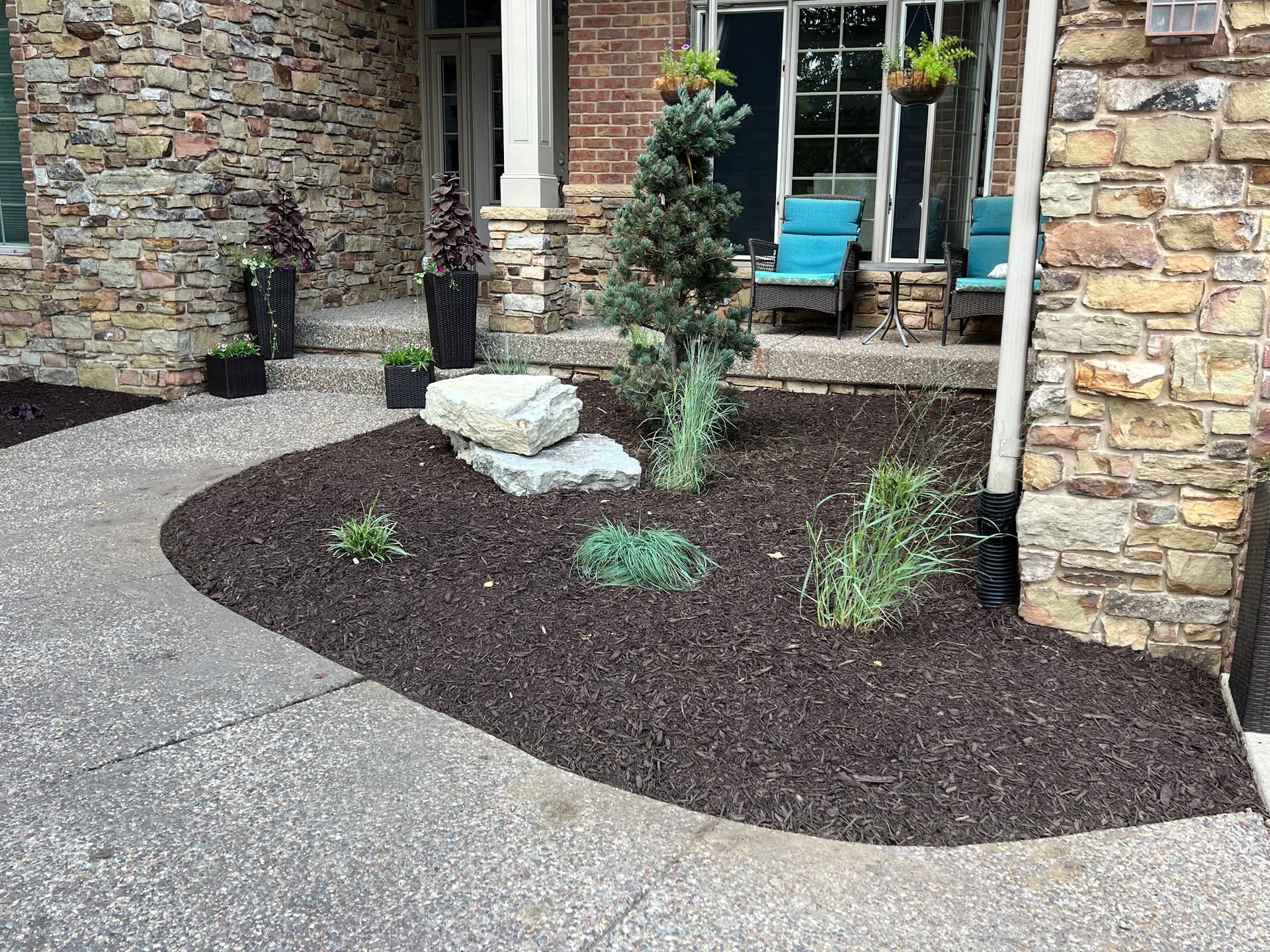 A landscaped front yard with dark mulch, a stone walkway, and a brick and stone facade.