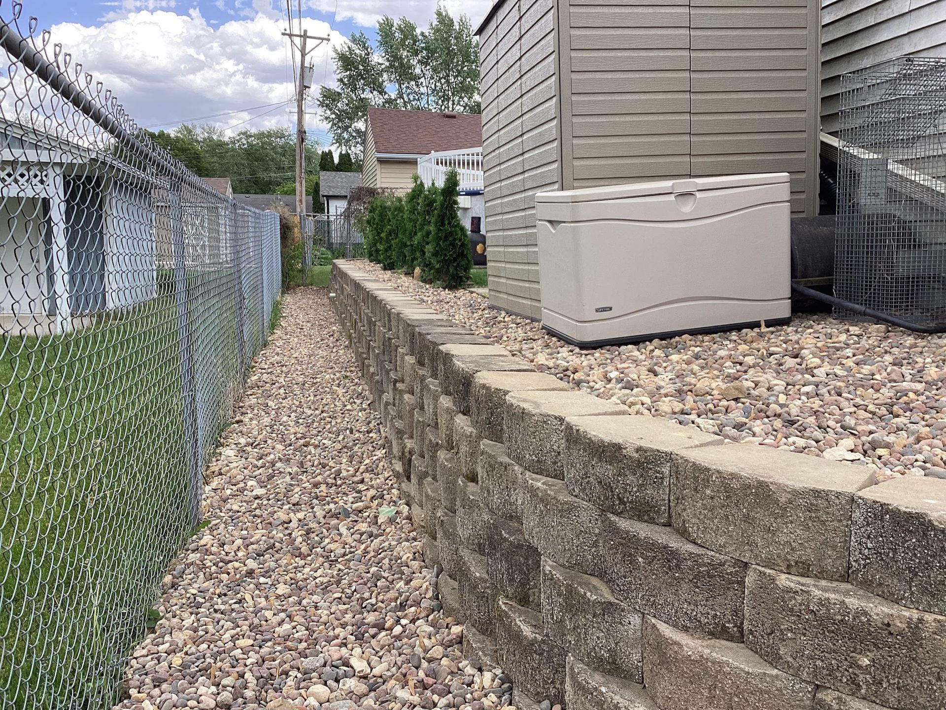 Backyard with a retaining wall, chain-link fence, shed, and gravel path.