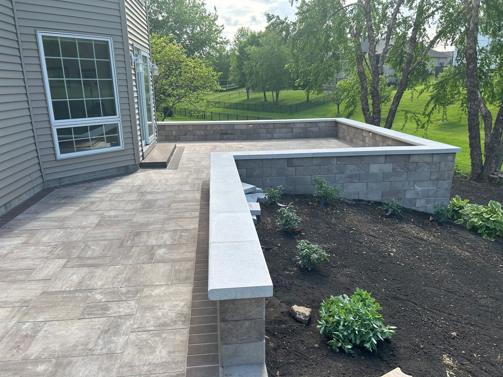 Stone patio with low retaining wall, next to a house and garden bed.