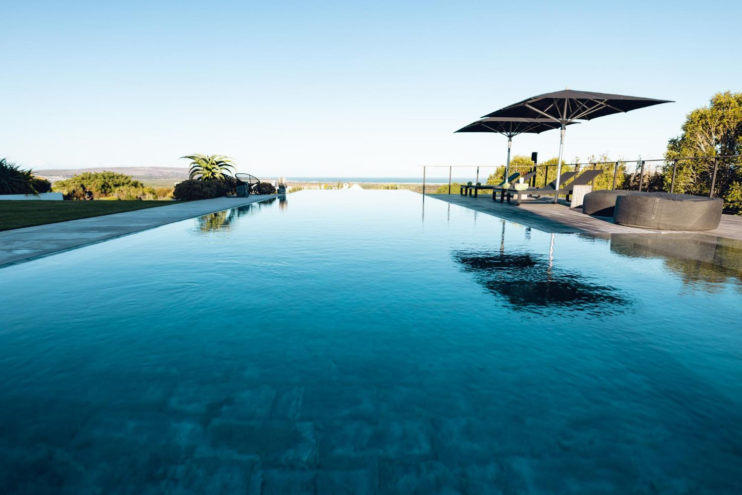 A very long swimming pool with two umbrellas in the background.