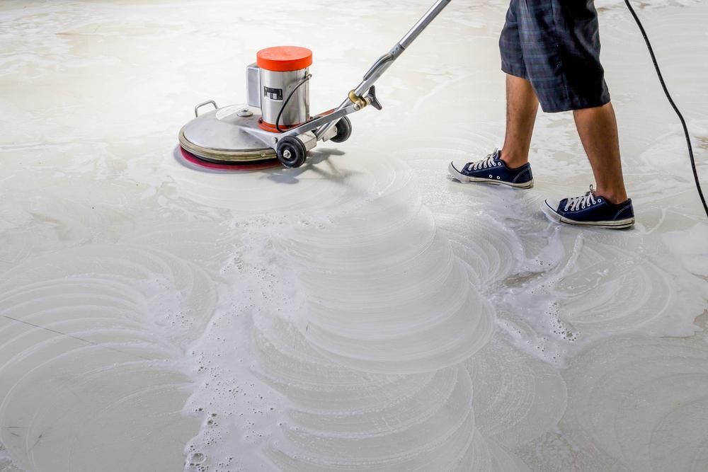 A Man is Cleaning a Concrete Floor With a Machine — South Pacific Cleaning in Bentley Park, QLD
