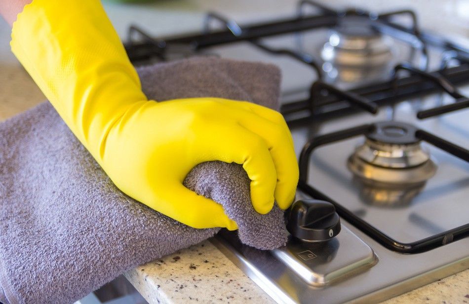 A Person Wearing Yellow Gloves is Cleaning a Stove Top With a Towel — South Pacific Cleaning in Bentley Park, QLD
