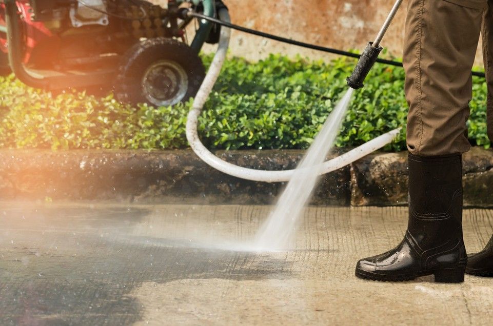 A Person is Using a High Pressure Washer to Clean a Sidewalk — South Pacific Cleaning in Bentley Park, QLD