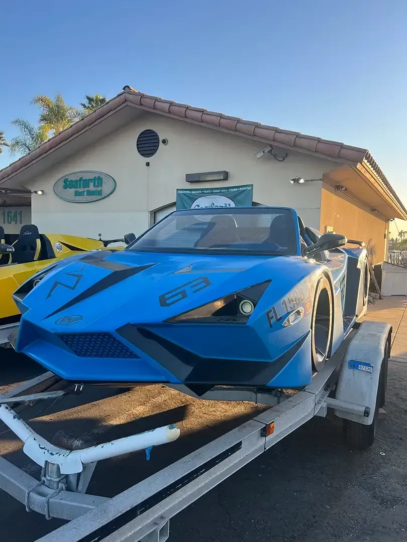 A blue sports car is on a trailer in front of a building