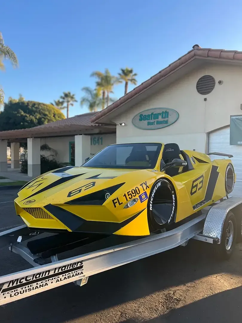 A yellow race car is on a trailer in front of a building