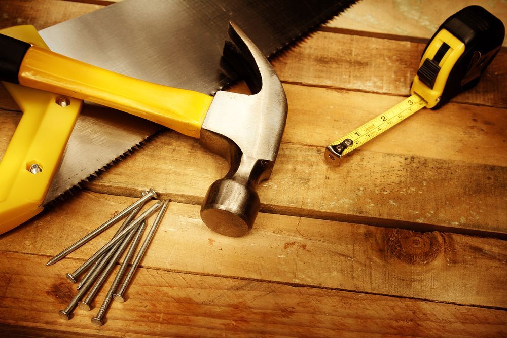 Hammer, nails, and tape measure on a wooden workbench with a yellow tool case