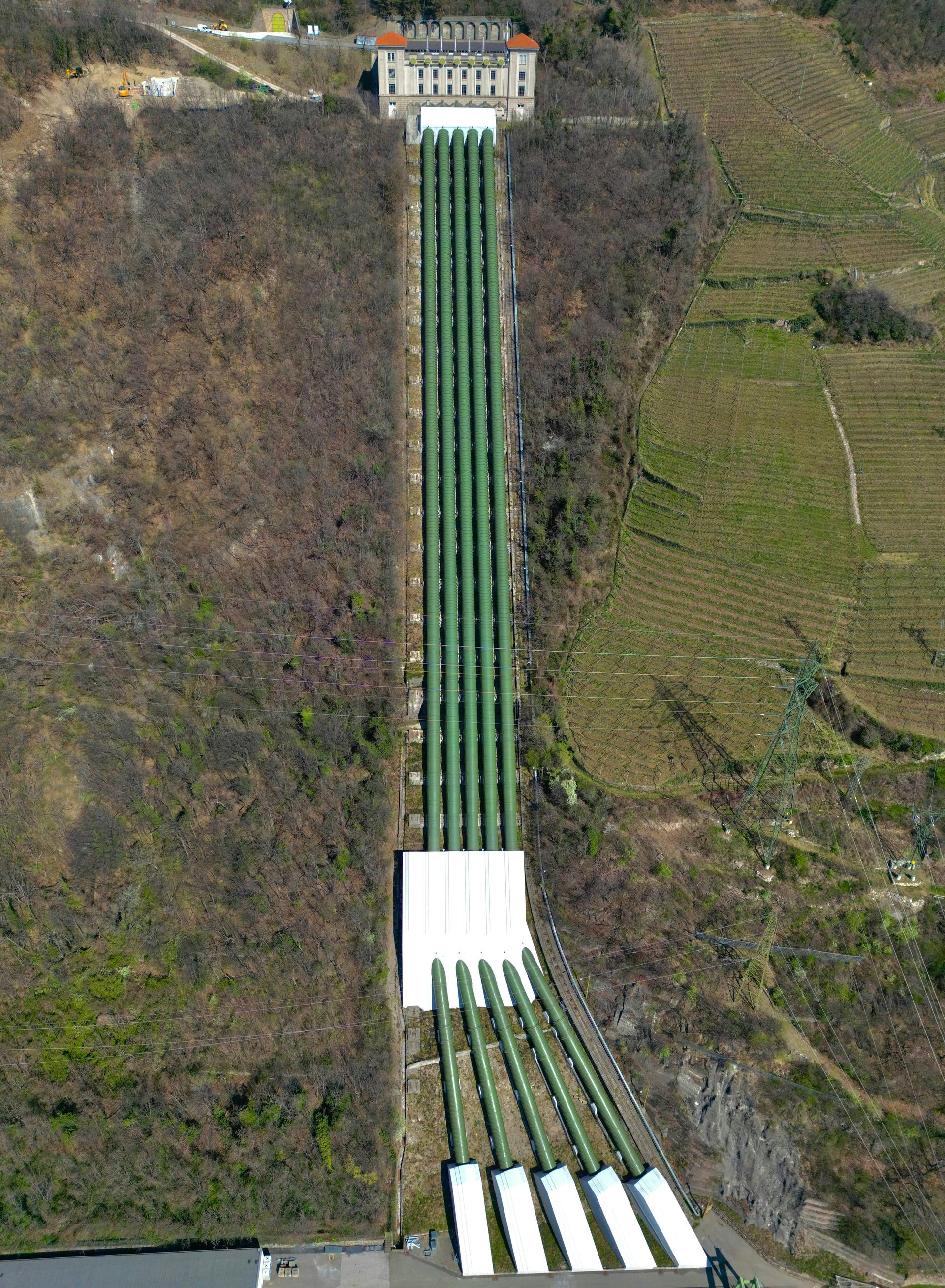 Hydroelectric plant with tall pipes running down a hillside to a white building.