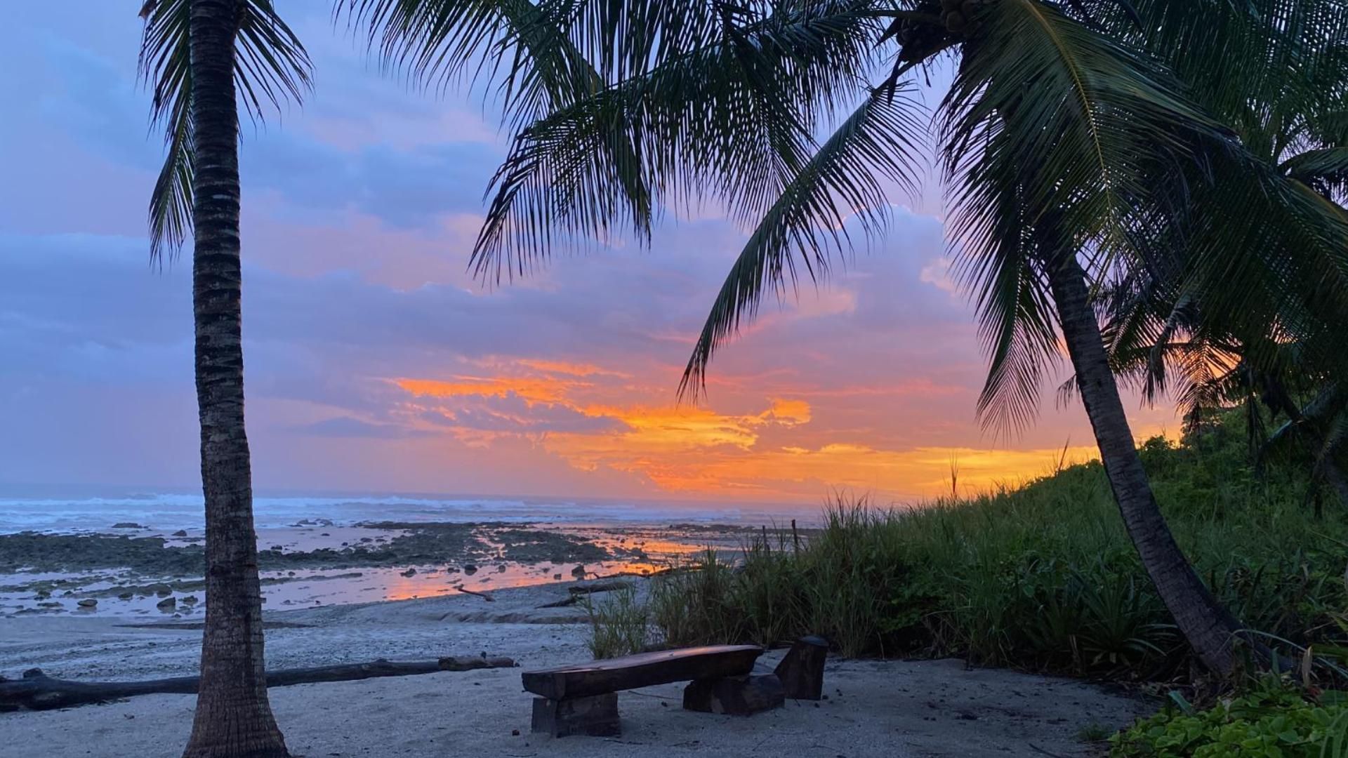 A sunset over a beach with a bench in the foreground