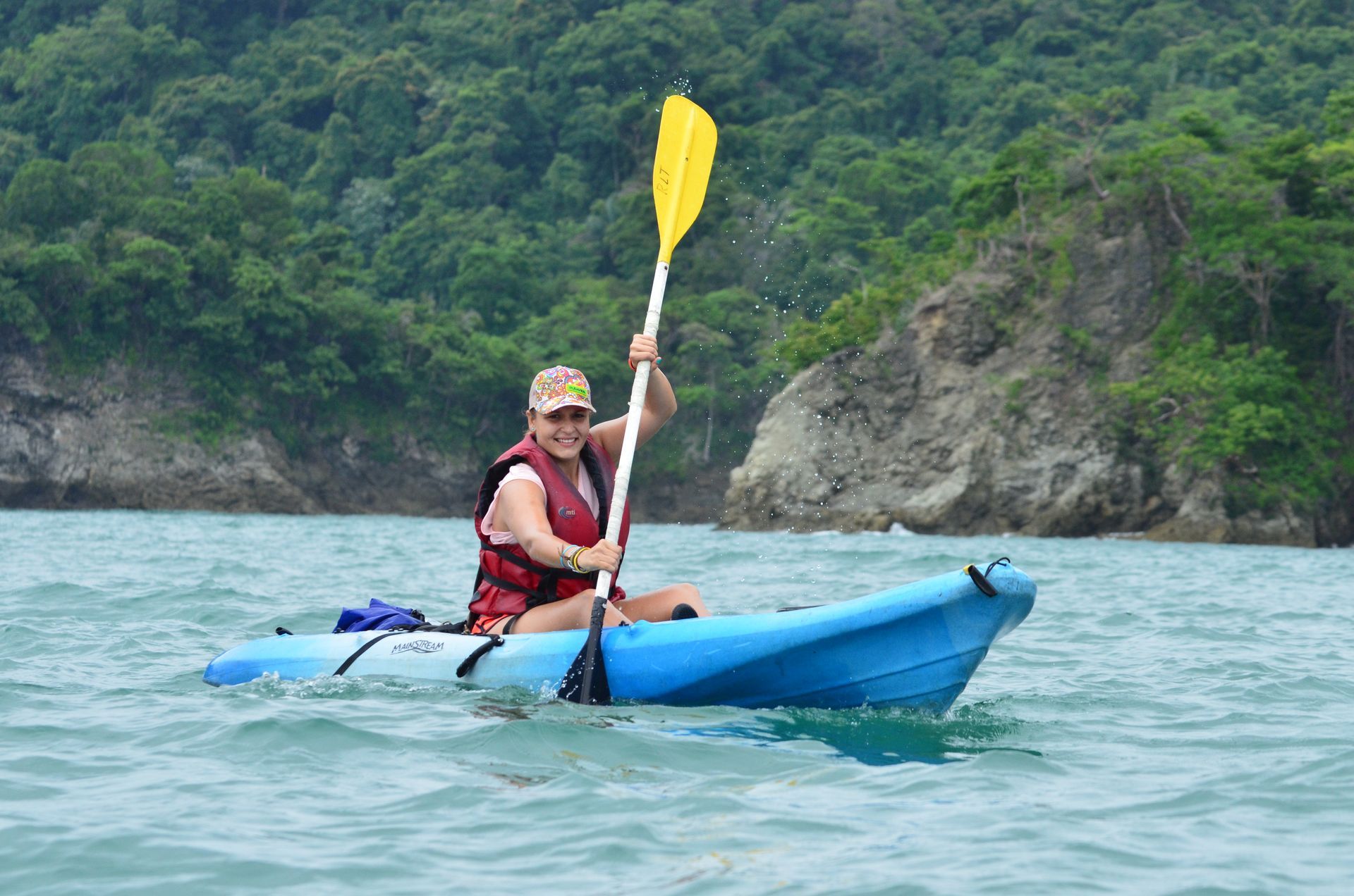 A woman is paddling a blue kayak in the ocean.