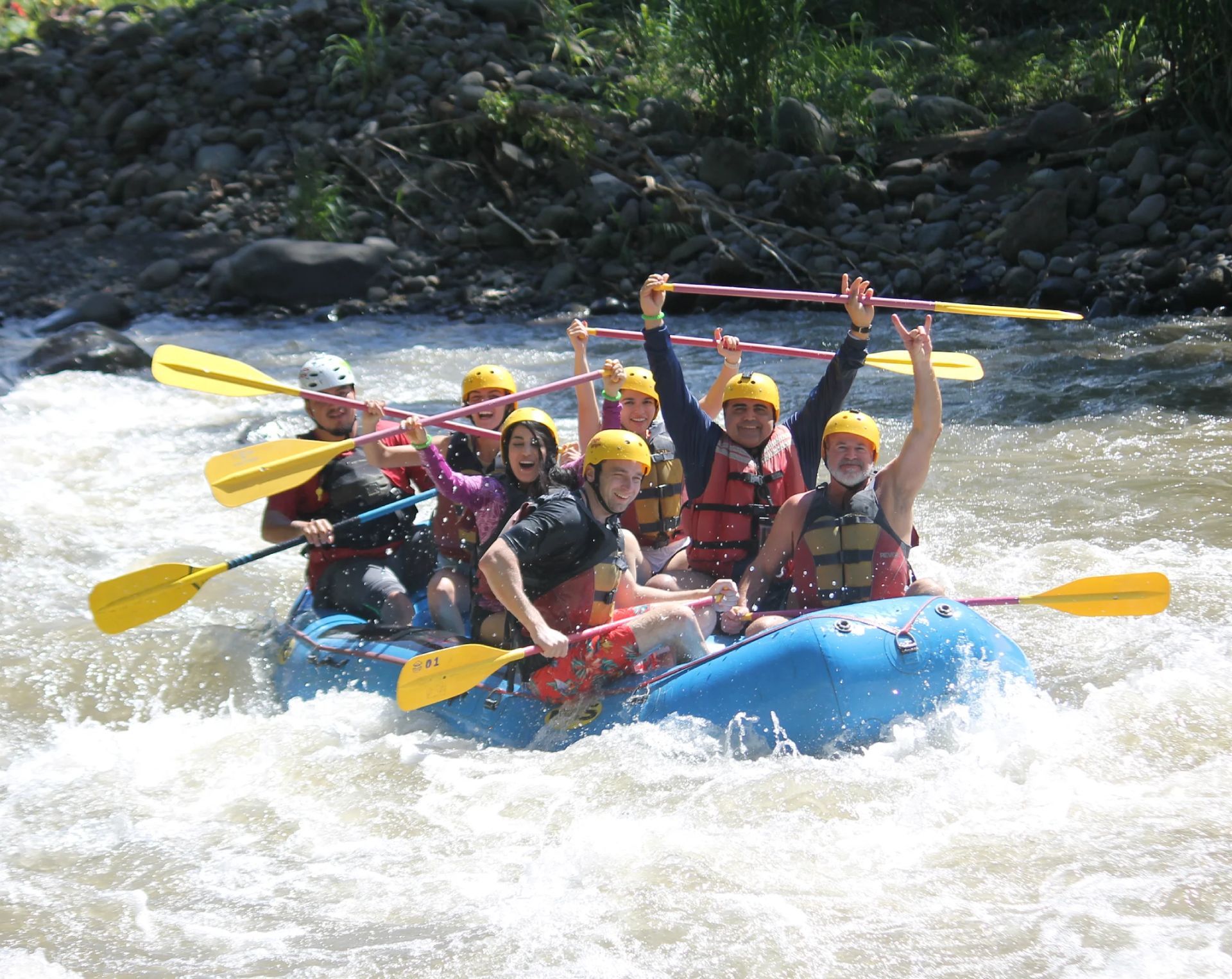 A group of people are rafting down a river with their arms in the air