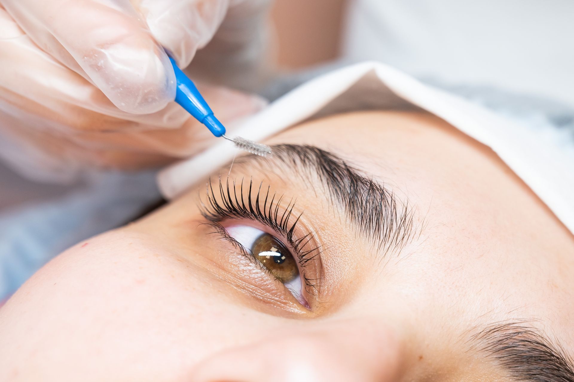 Close-up of a person's eye and eyebrow receiving eyebrow shaping treatment with a small blue tool.