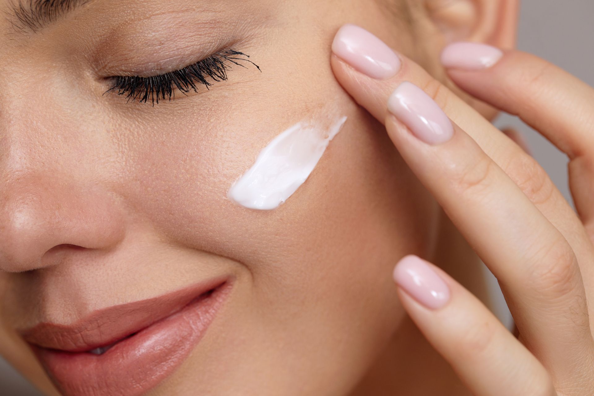 Woman applying white cream to her cheek with a smile.