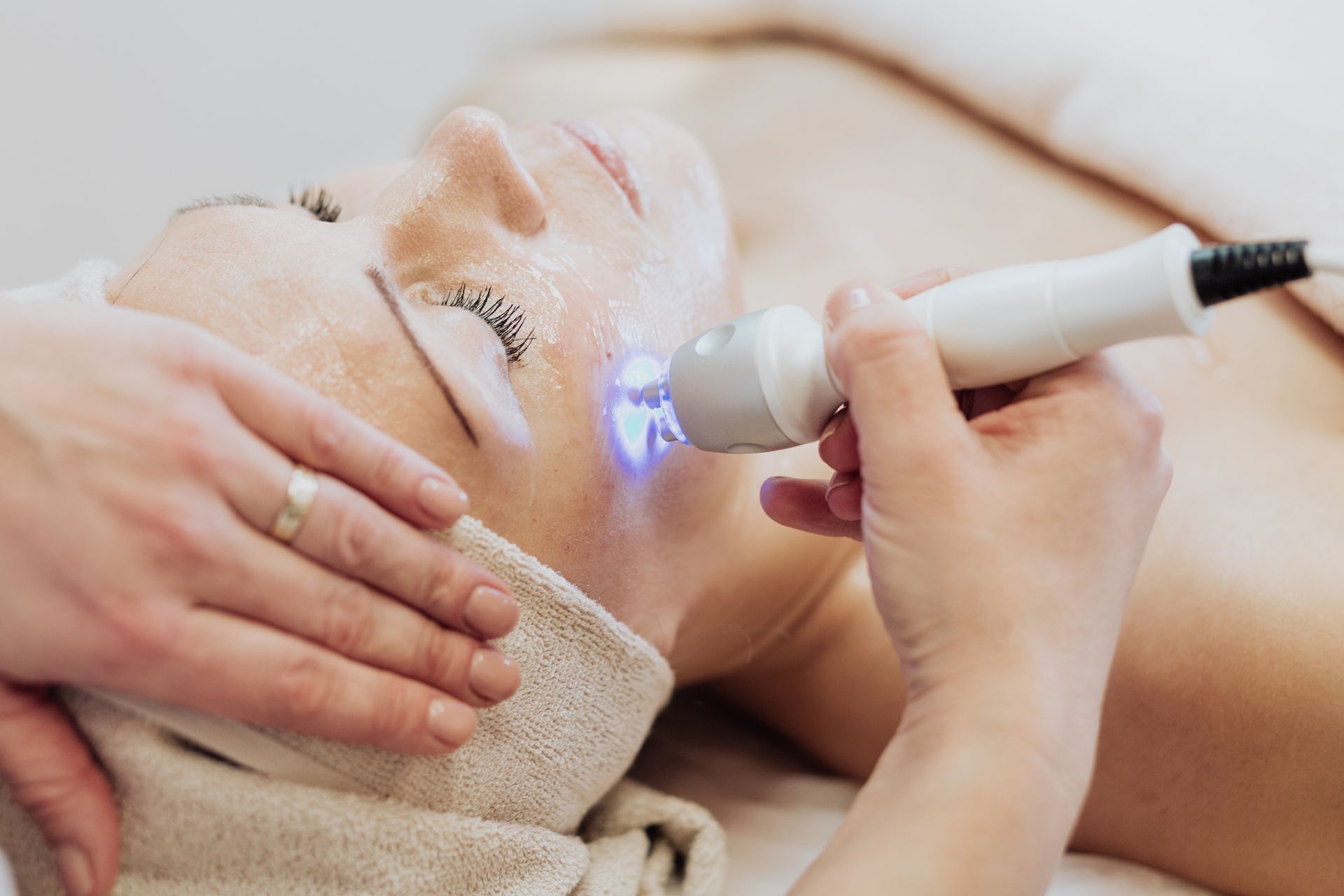 Person receiving a facial treatment, a device emits blue light on their face.