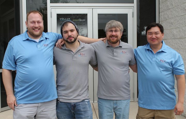 Four men are posing for a picture in front of a building