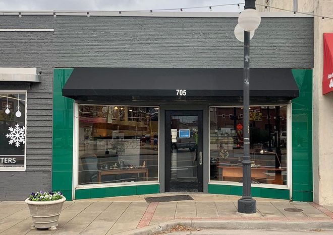 A store front with a black awning and a potted plant in front of it.