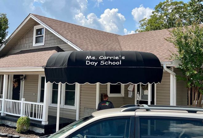 A car is parked in front of a house with a black awning.