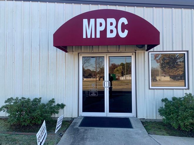 A white building with a red awning that says mpbc