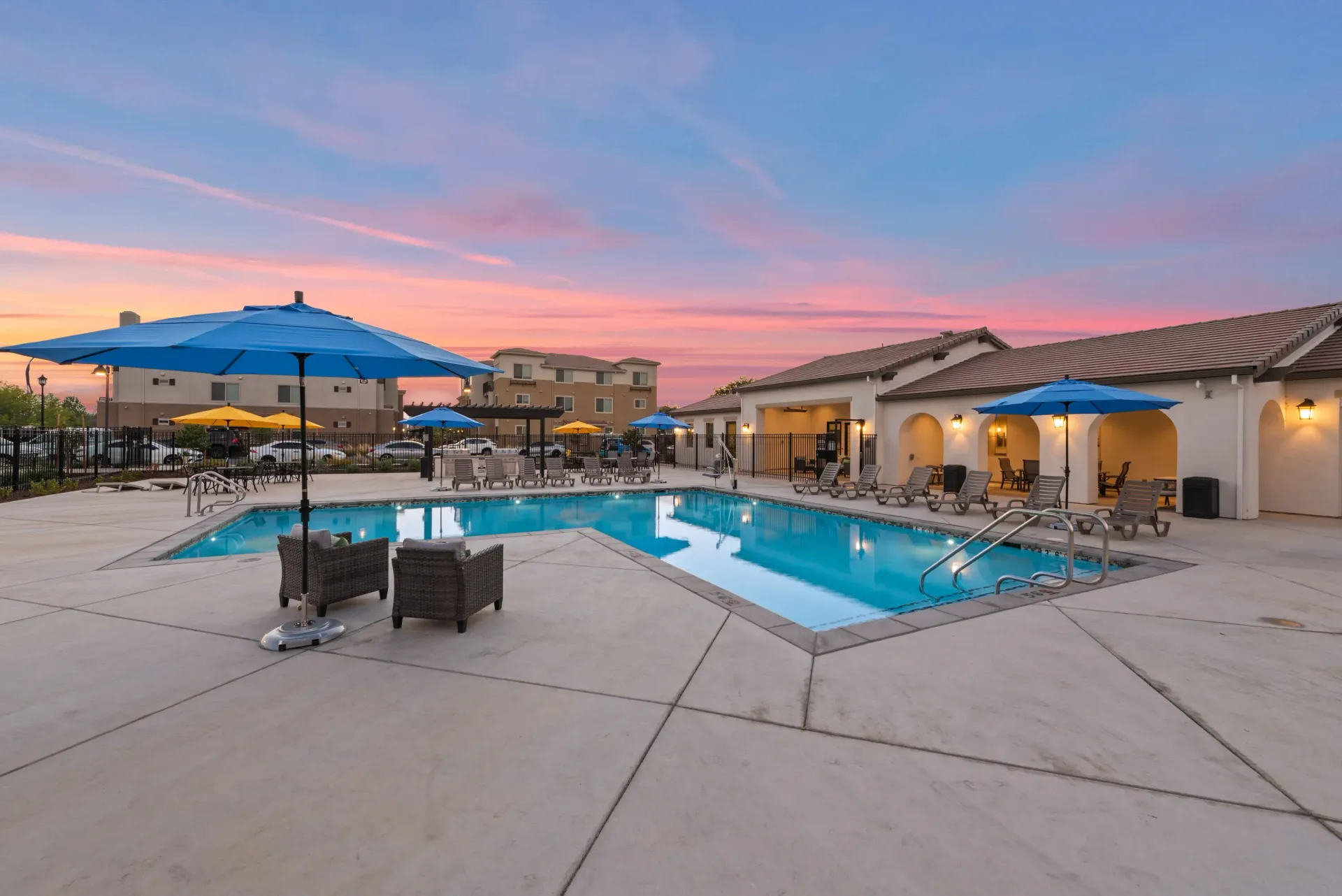 Outdoor community pool at an apartment complex with blue umbrellas and lounge chairs at sunset. Take a closer look at Silvergate living.