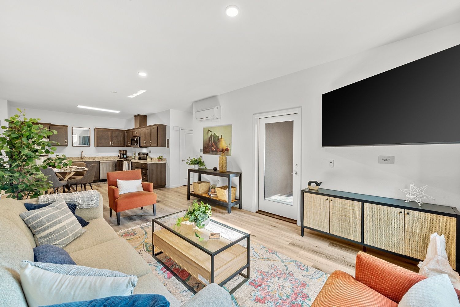 Open-concept living area with sofa, orange chairs, coffee table, and a kitchen in the background. Find your rhythm at The Silvergate.