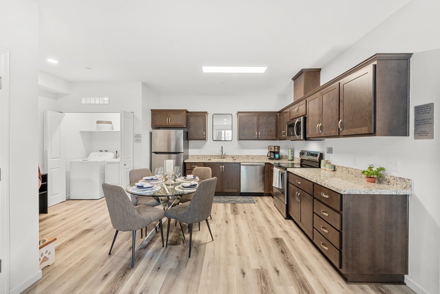 Open kitchen with dark wood cabinets, granite countertops, stainless steel appliances, and a round glass dining table. See why Brentwood feels like home here.