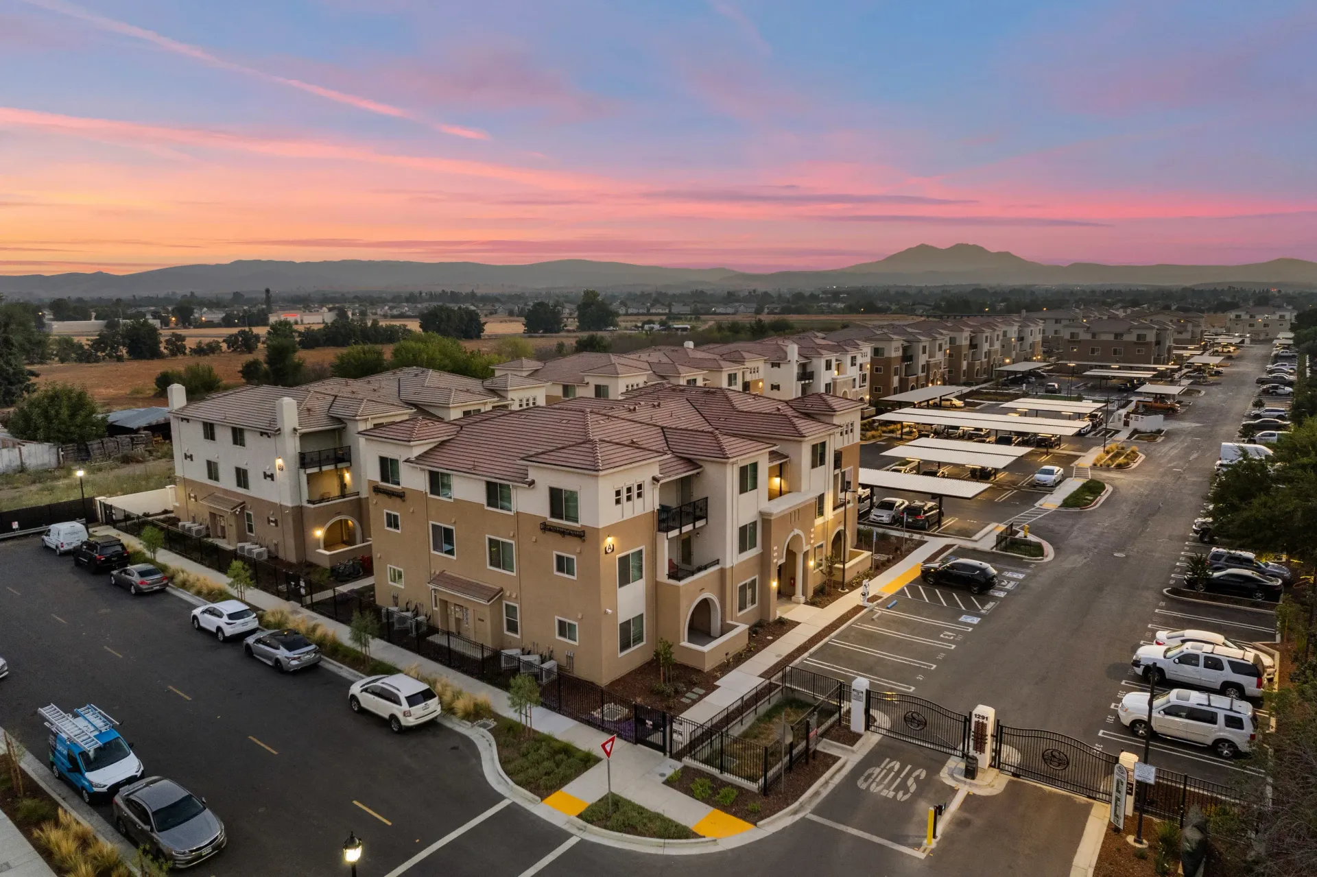 Aerial view of a modern apartment complex with parking lots at sunset. Explore life at The Silvergate in Brentwood, CA.