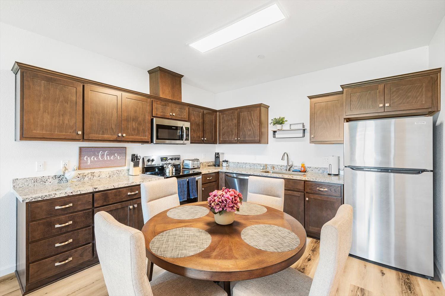 Apartment kitchen with dark wood cabinets, granite countertops, stainless appliances, and a round dining table. Take a peek inside Silvergate living.