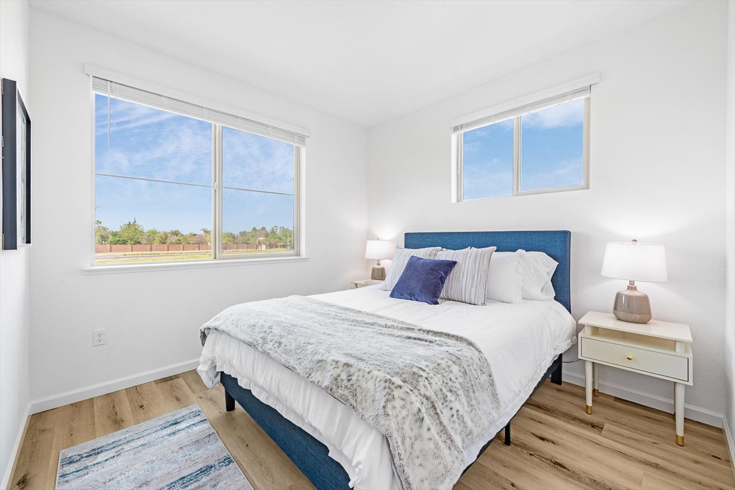 Bright bedroom with a blue upholstered bed, white walls, two nightstands, and large windows. Start your next chapter at The Silvergate.