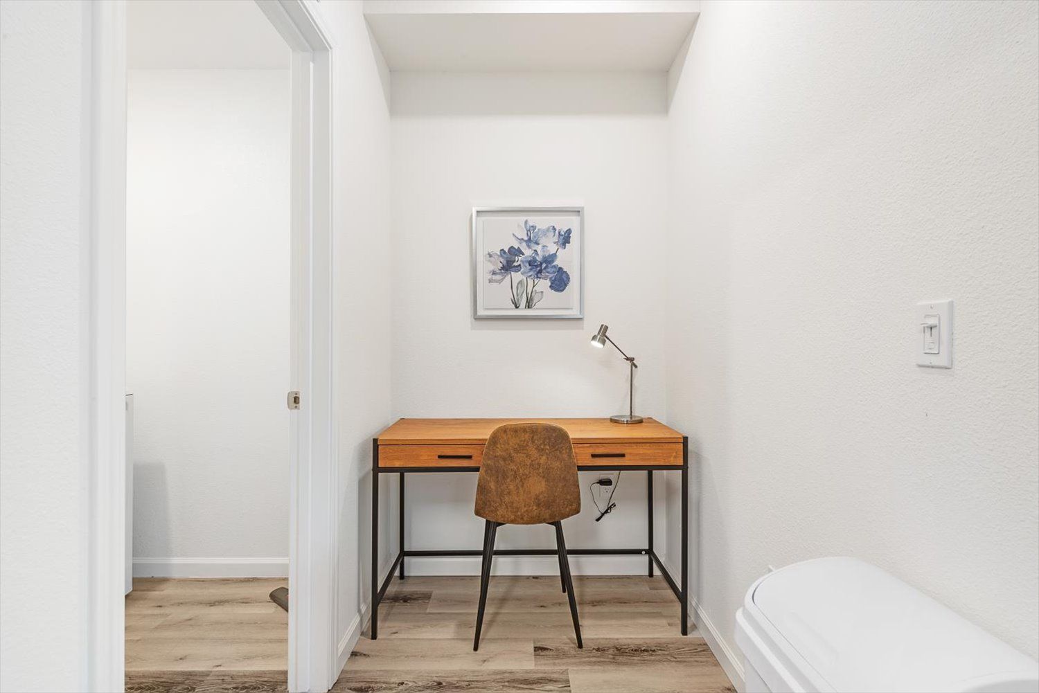 Small home office nook with a wooden desk, brown chair, and a desk lamp against white walls. Learn more about life at Silvergate.