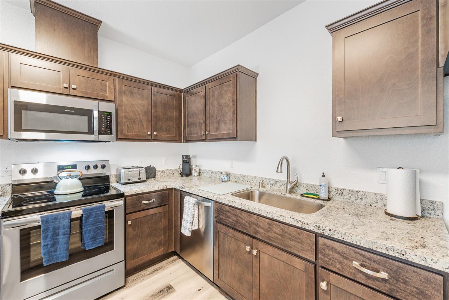 Kitchen with granite countertops, brown cabinets, stainless steel stove and microwave, sink. Find your space at The Silvergate community.