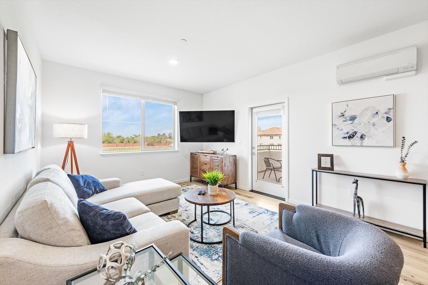 Bright living room with beige sectional sofa, blue pillows, TV, and glass door to balcony. Explore modern comfort in Brentwood, CA.