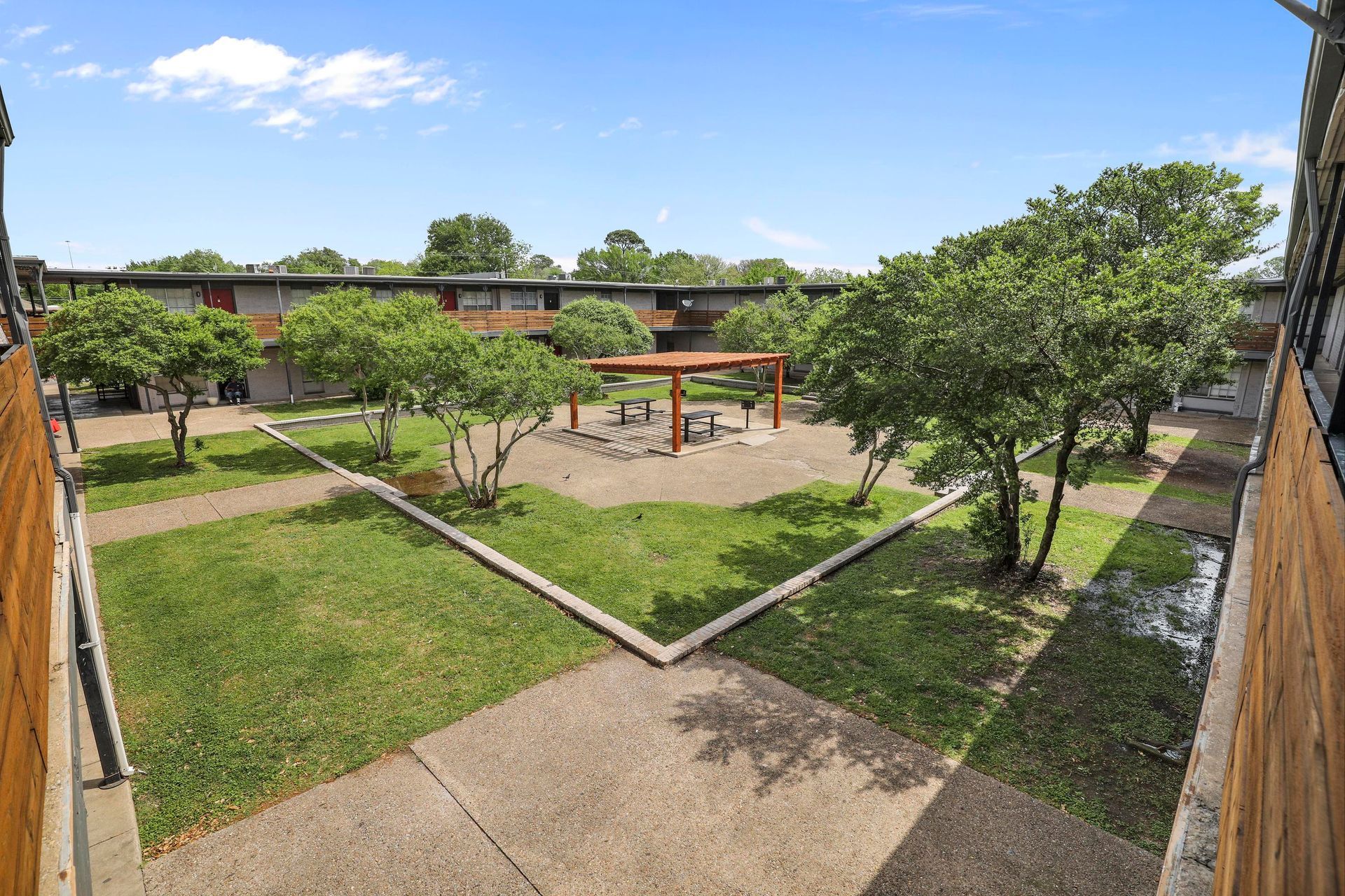 Courtyard with green grass, trees, and a wooden pergola, surrounded by apartment buildings.