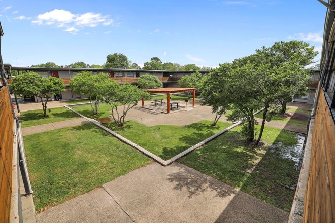 Courtyard with green grass, trees, and a wooden pergola, surrounded by apartment buildings.