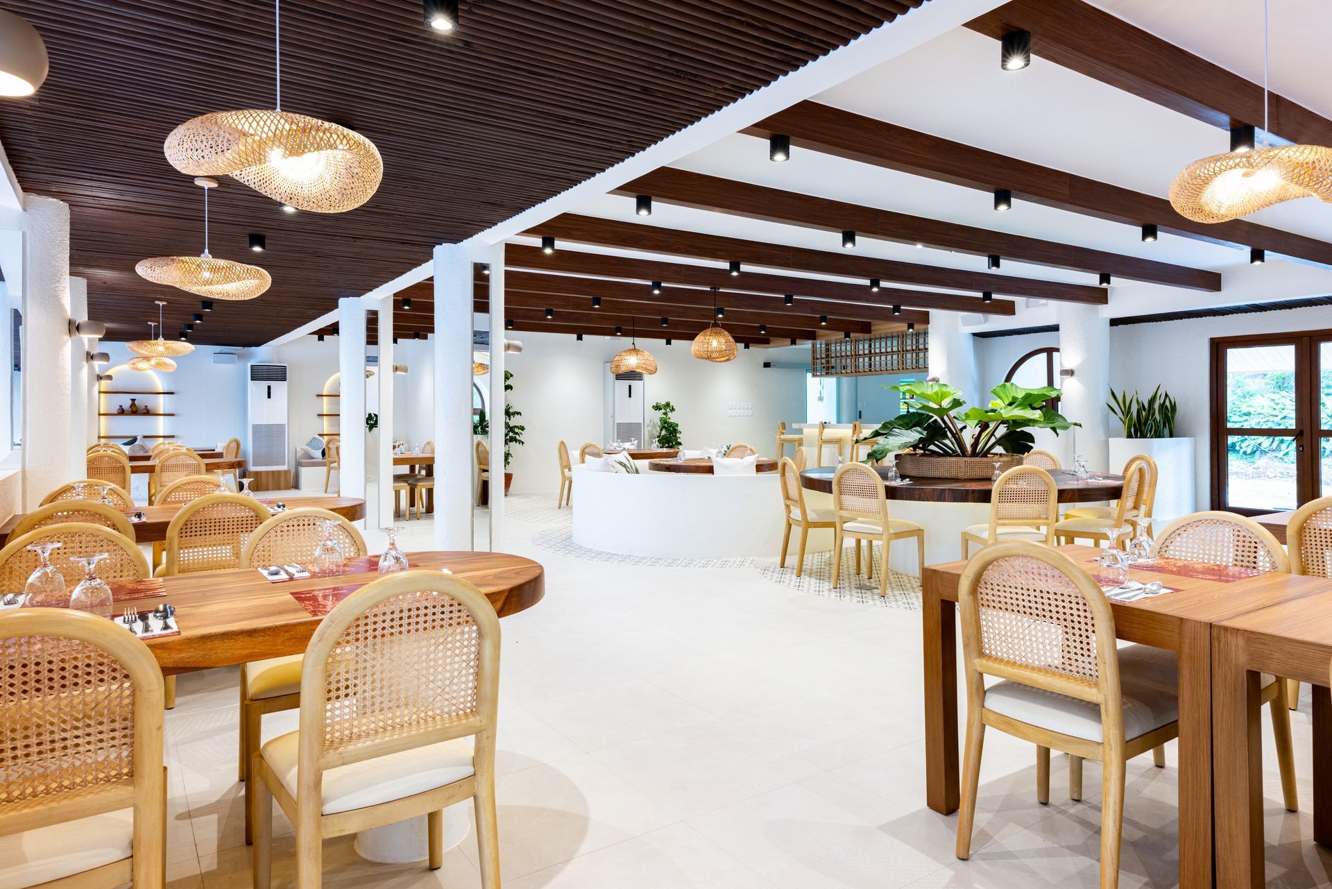 Bright, airy café interior with wicker chairs, wooden tables, and a white counter under exposed beams