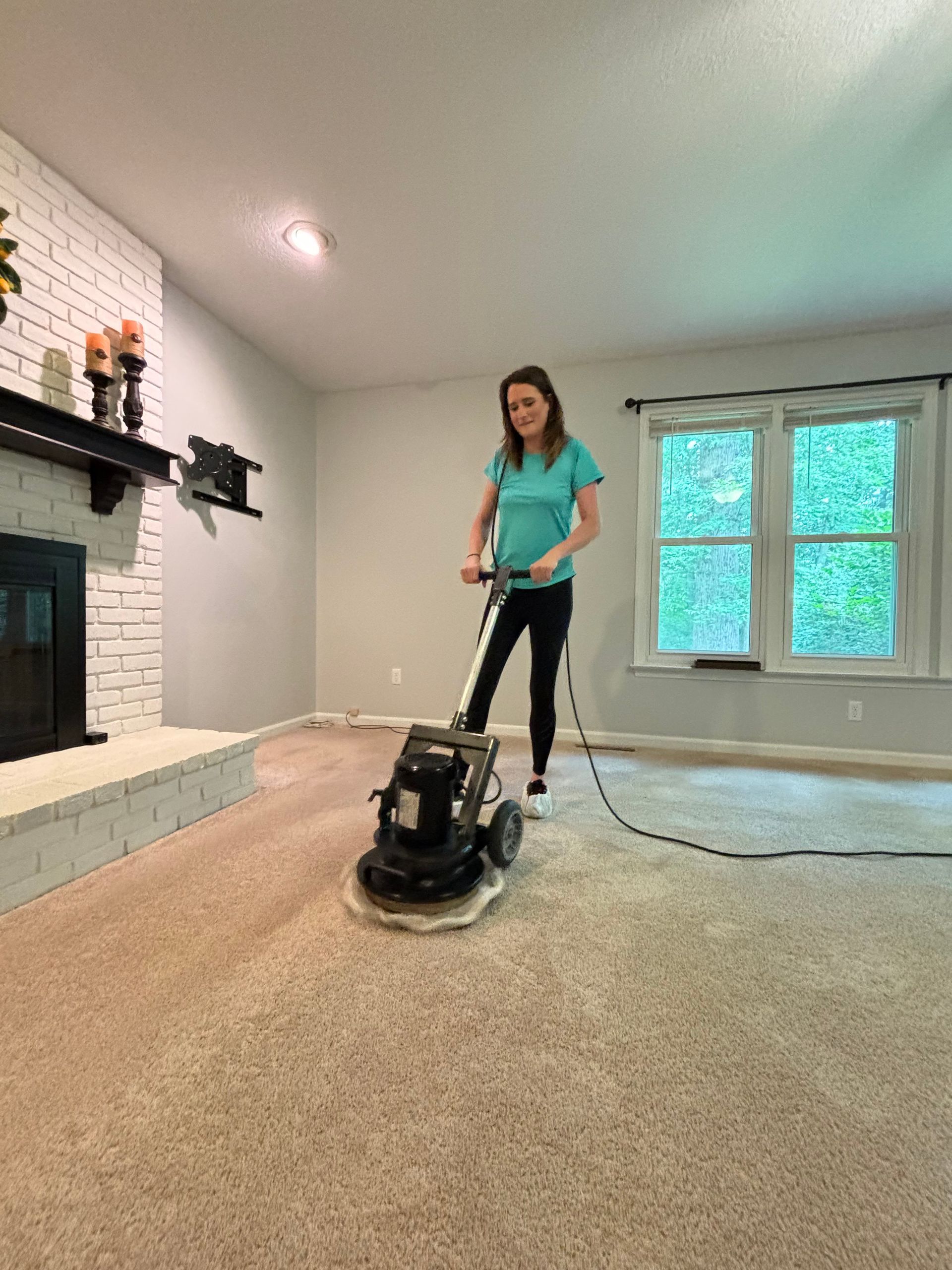 A woman is using a machine to clean a carpet in a living room.