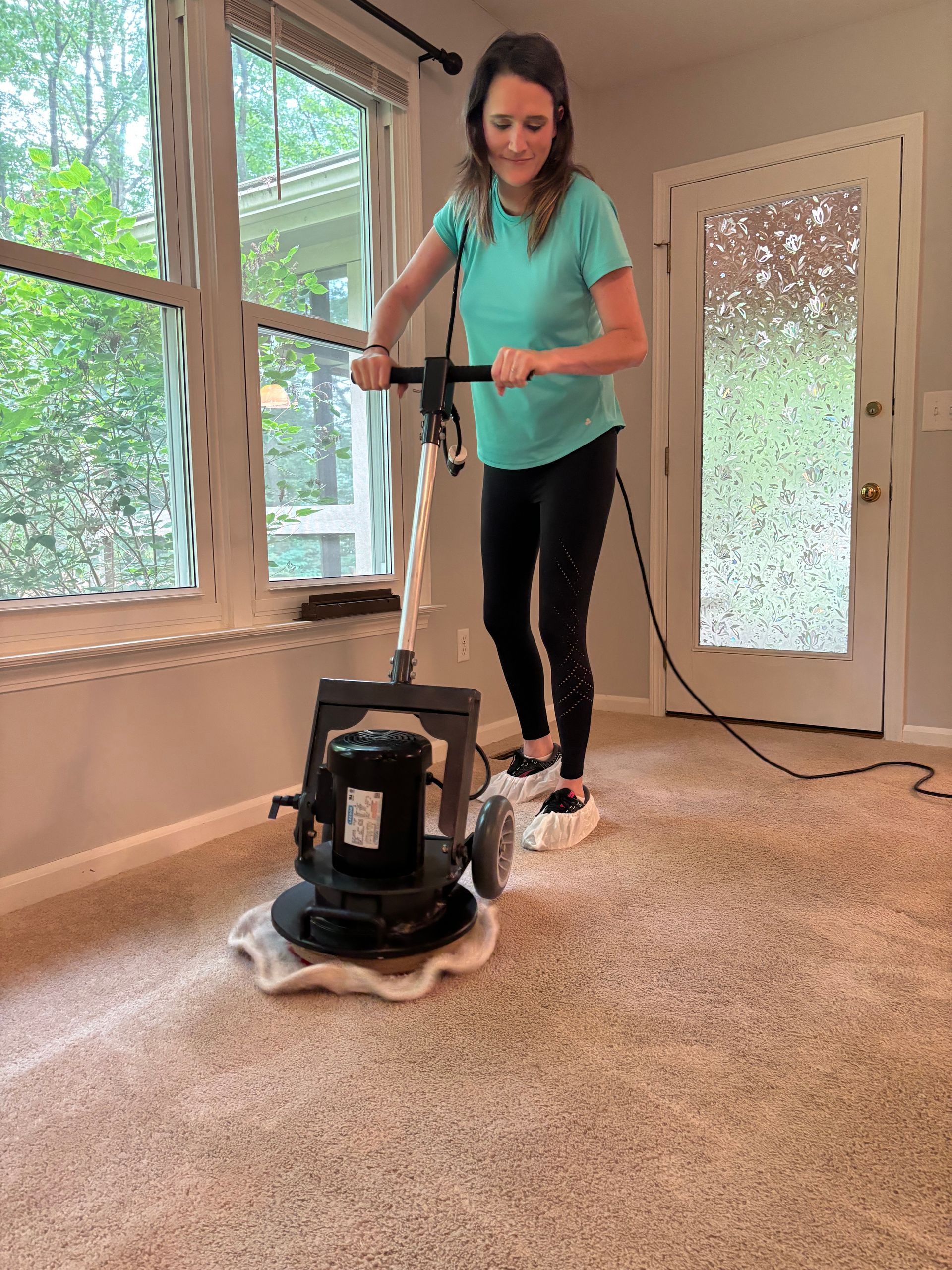 A woman is using a machine to clean a carpet in a living room.
