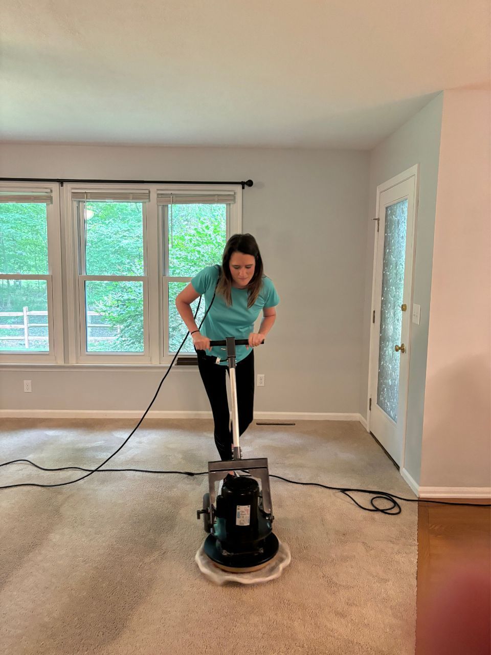 A woman is using a machine to clean a carpet in a living room.