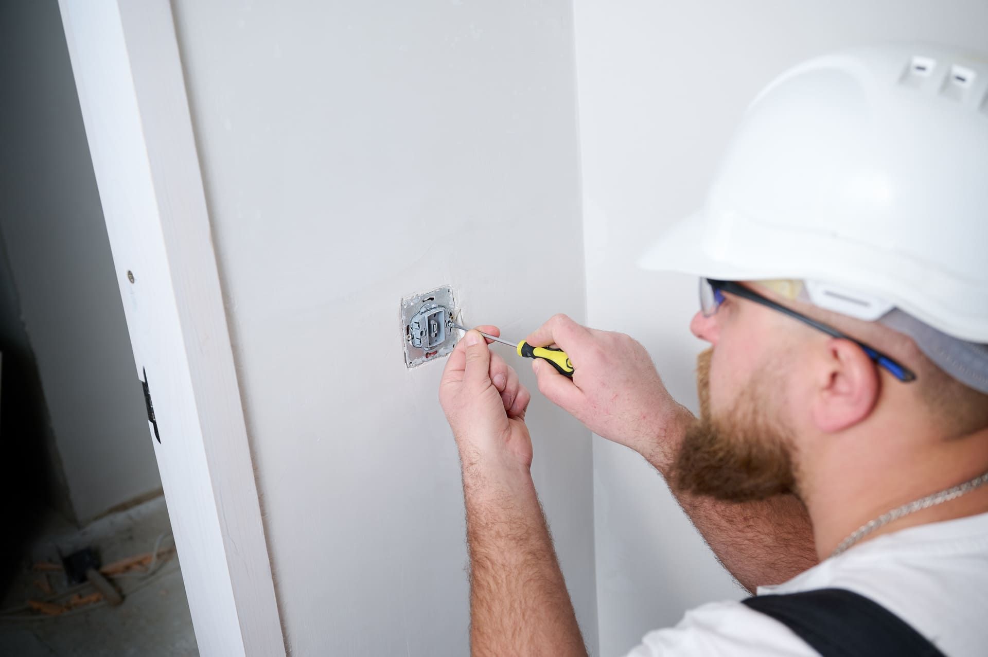 electrician installing electric socket using screwdriver at construction site. Power socket installation. Installing a power outlet in to a plastic box on a wall. 