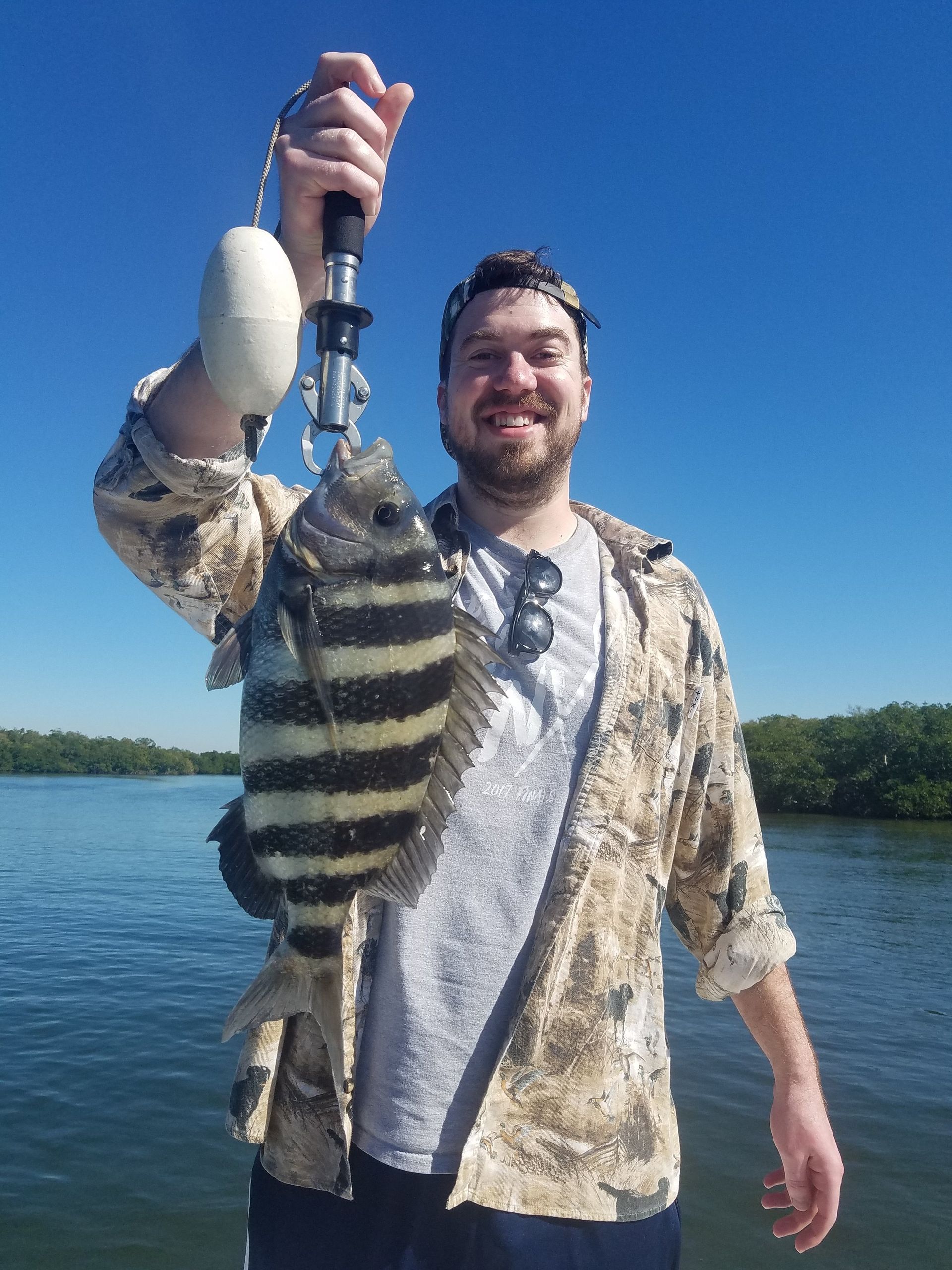 A man is holding a fish in his hand in front of a body of water.